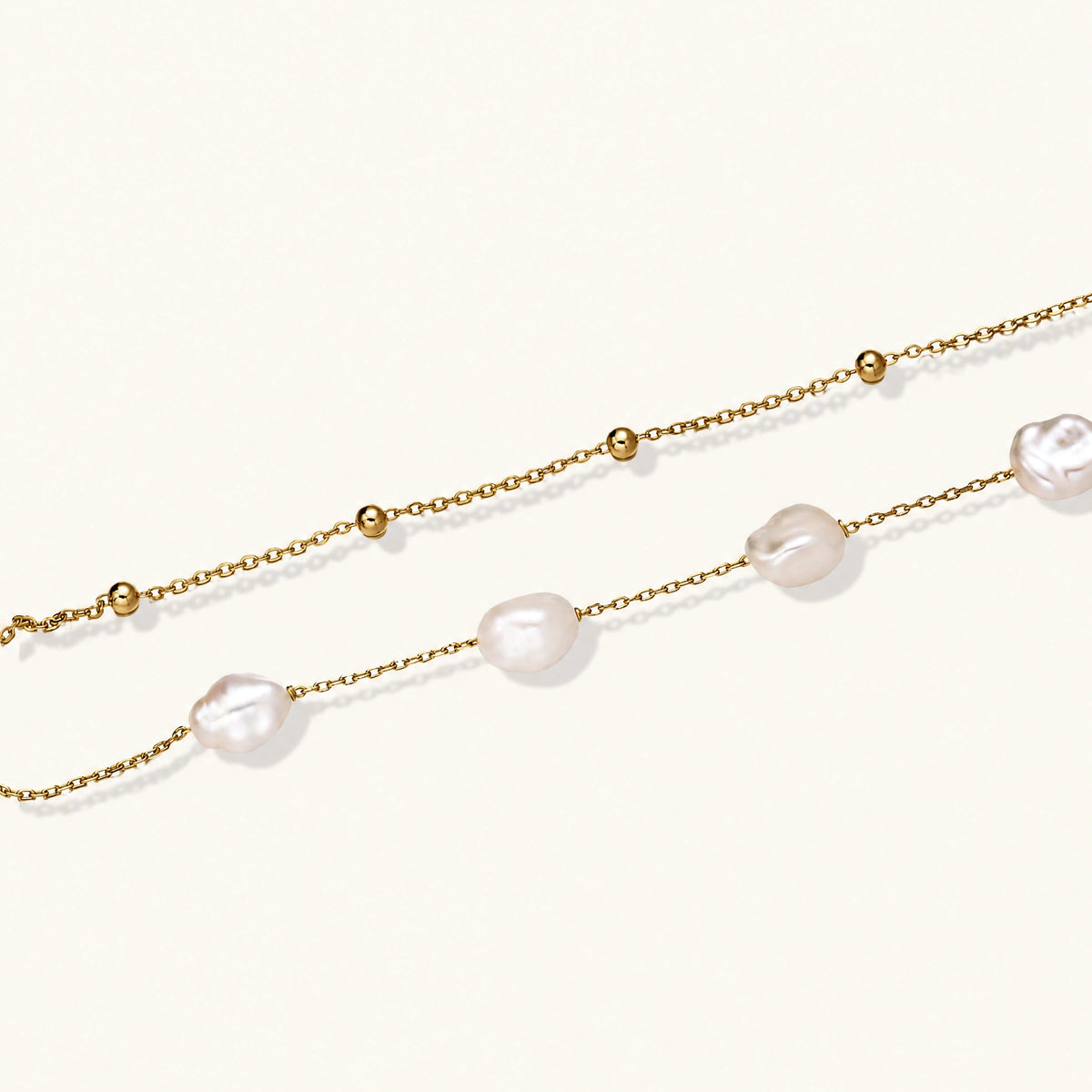 Double-strand gold bracelet with irregular baroque pearls and smooth freshwater pearls on cream background.