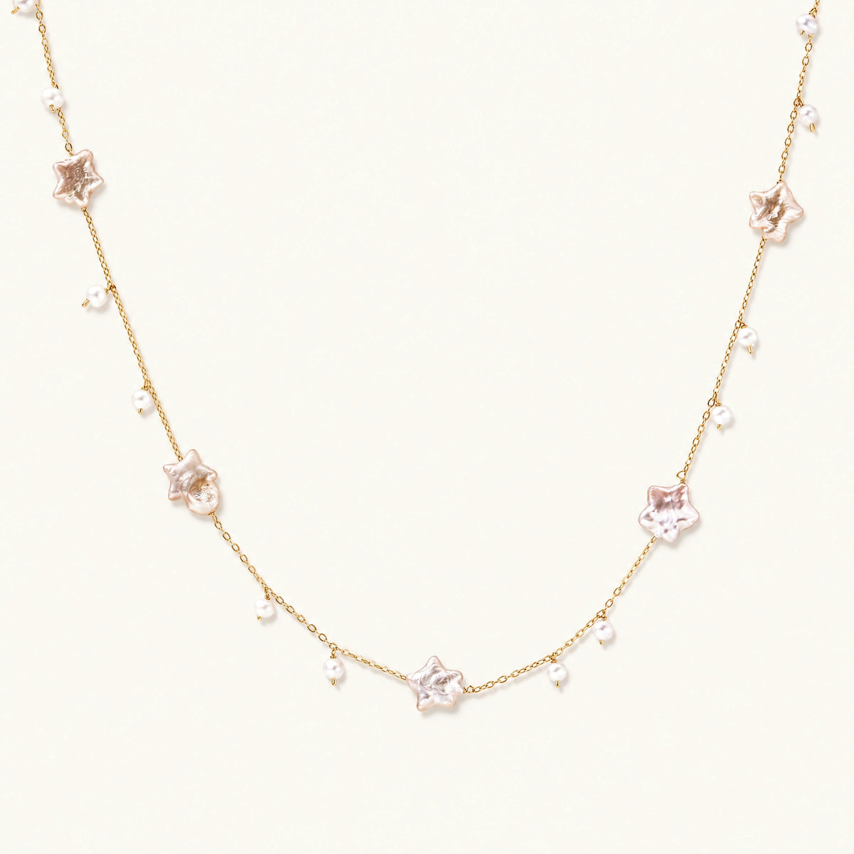 Gold vermeil chain with iridescent star-shaped baroque pearls and small round freshwater pearl drops on cream background.