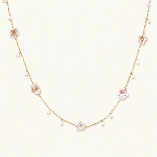 Gold vermeil chain with iridescent star-shaped baroque pearls and small round freshwater pearl drops on cream background.