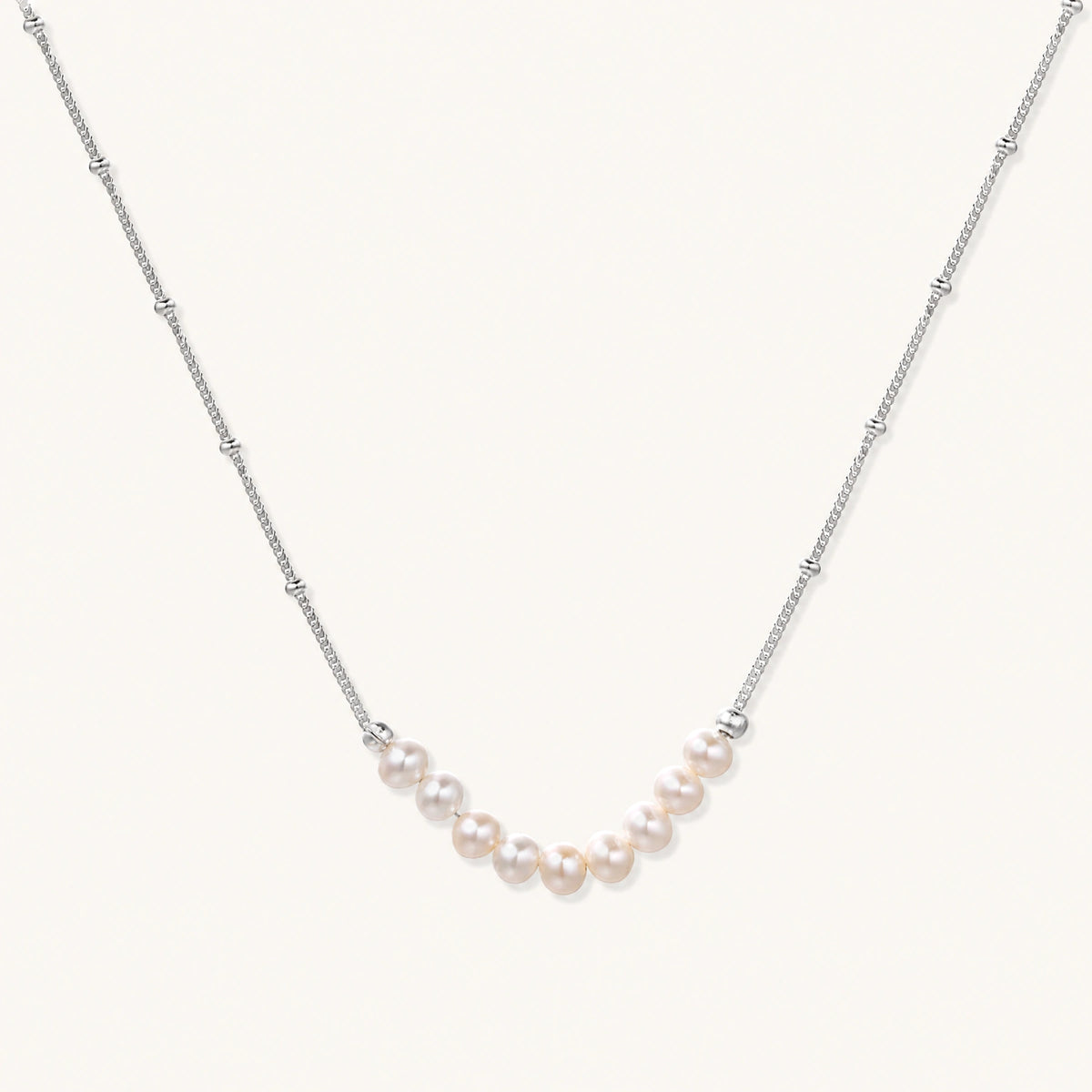 Delicate sterling silver chain necklace with small freshwater pearls arranged in a curved smile arc on cream background.