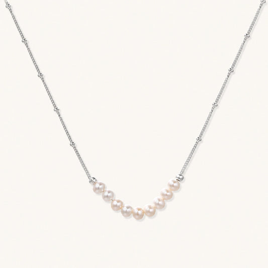 Delicate sterling silver chain necklace with small freshwater pearls arranged in a curved smile arc on cream background.