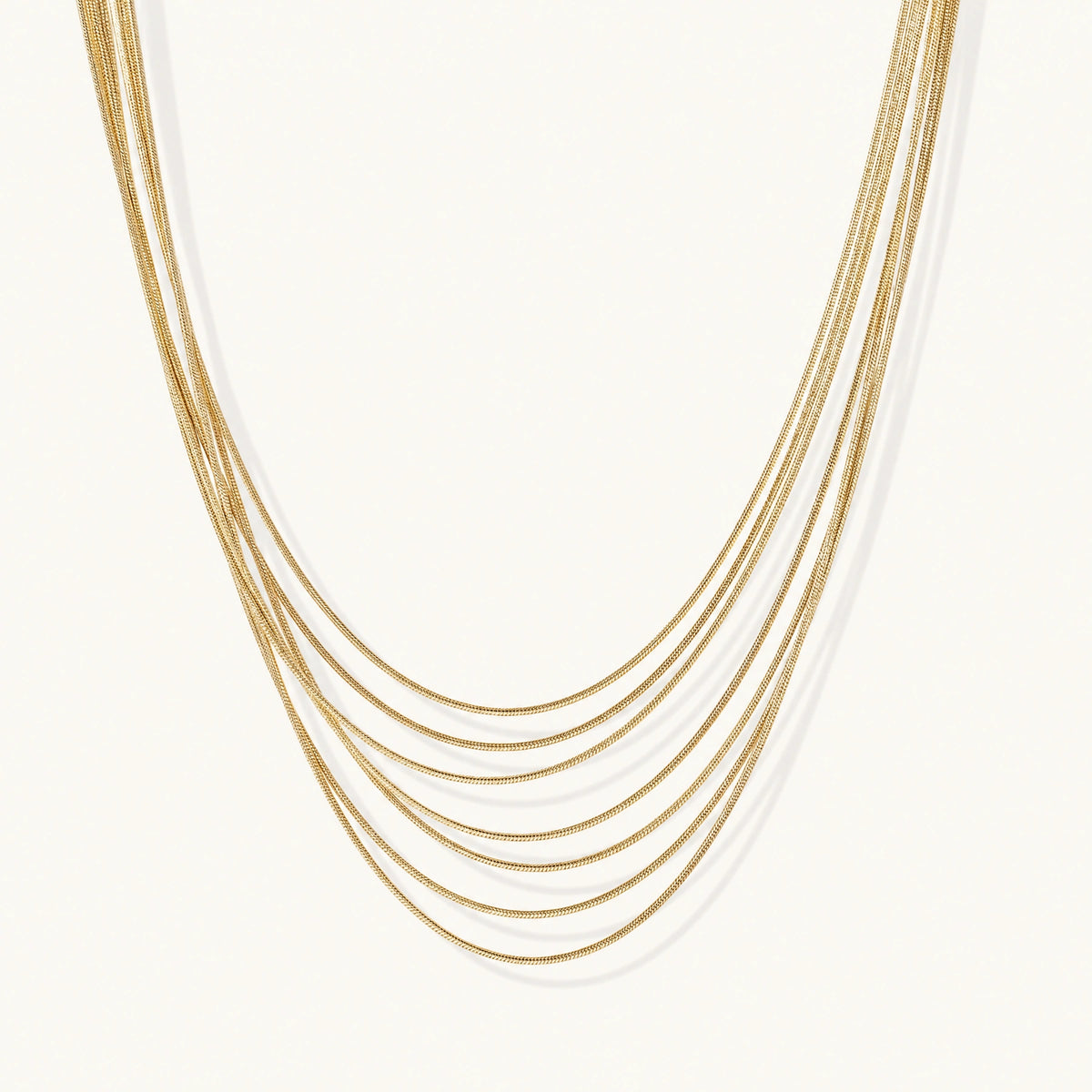 Seven delicate gold-plated snake chains create an elegant layered necklace on a neutral background.