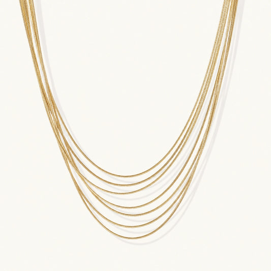 Seven delicate gold-plated snake chains create an elegant layered necklace on a neutral background.