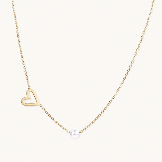 Dainty 14K gold plated stainless steel necklace with an open heart charm and a single round white bead on a cream background.