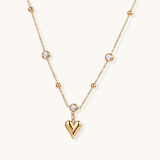 Delicate gold-plated necklace with bezel-set crystals and small heart pendant on beige background