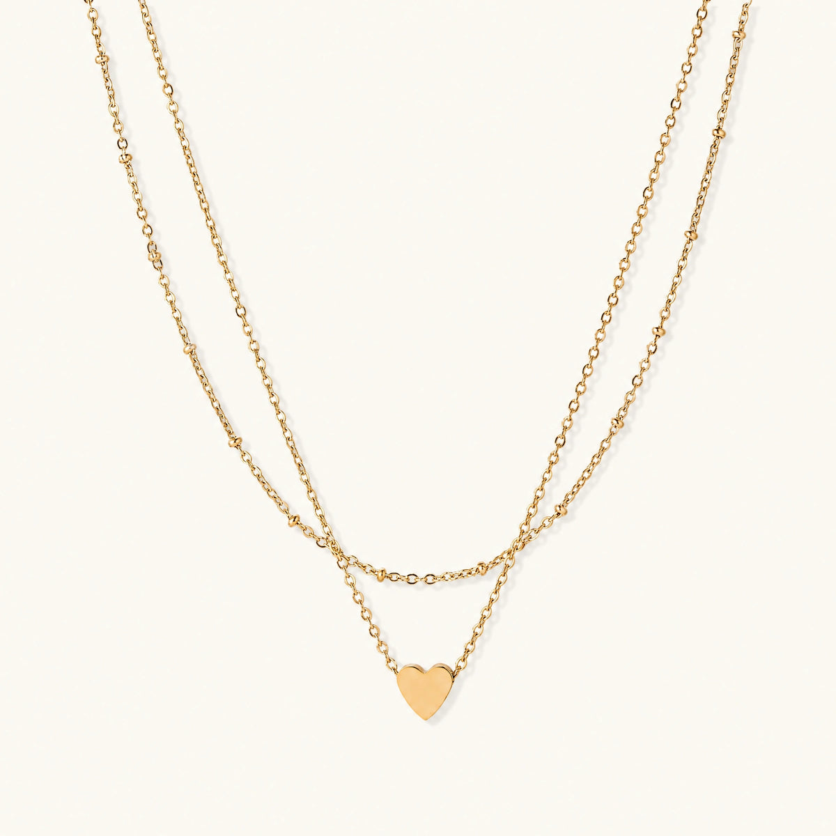 Delicate double-chain gold necklace with tiny heart pendant on cream background