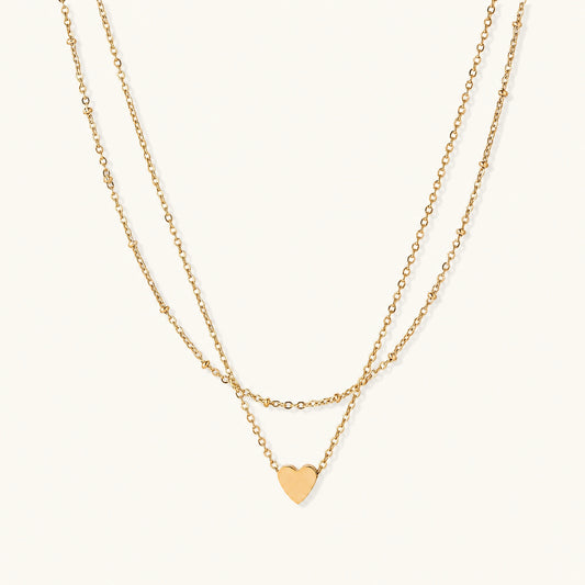 Delicate double-chain gold necklace with tiny heart pendant on cream background