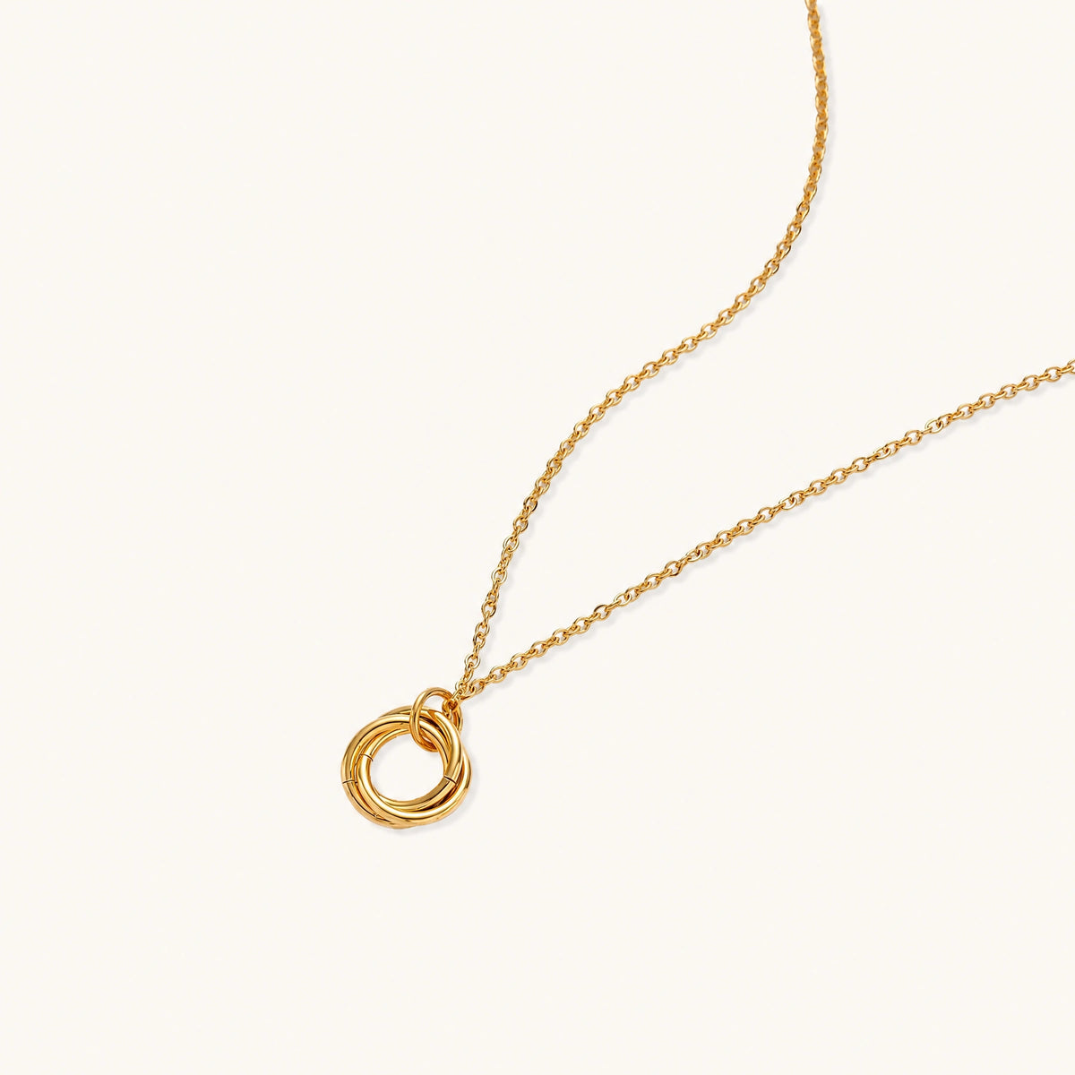 Delicate gold-plated necklace with three interlocking circle rings forming a minimalist knot pendant on cream background