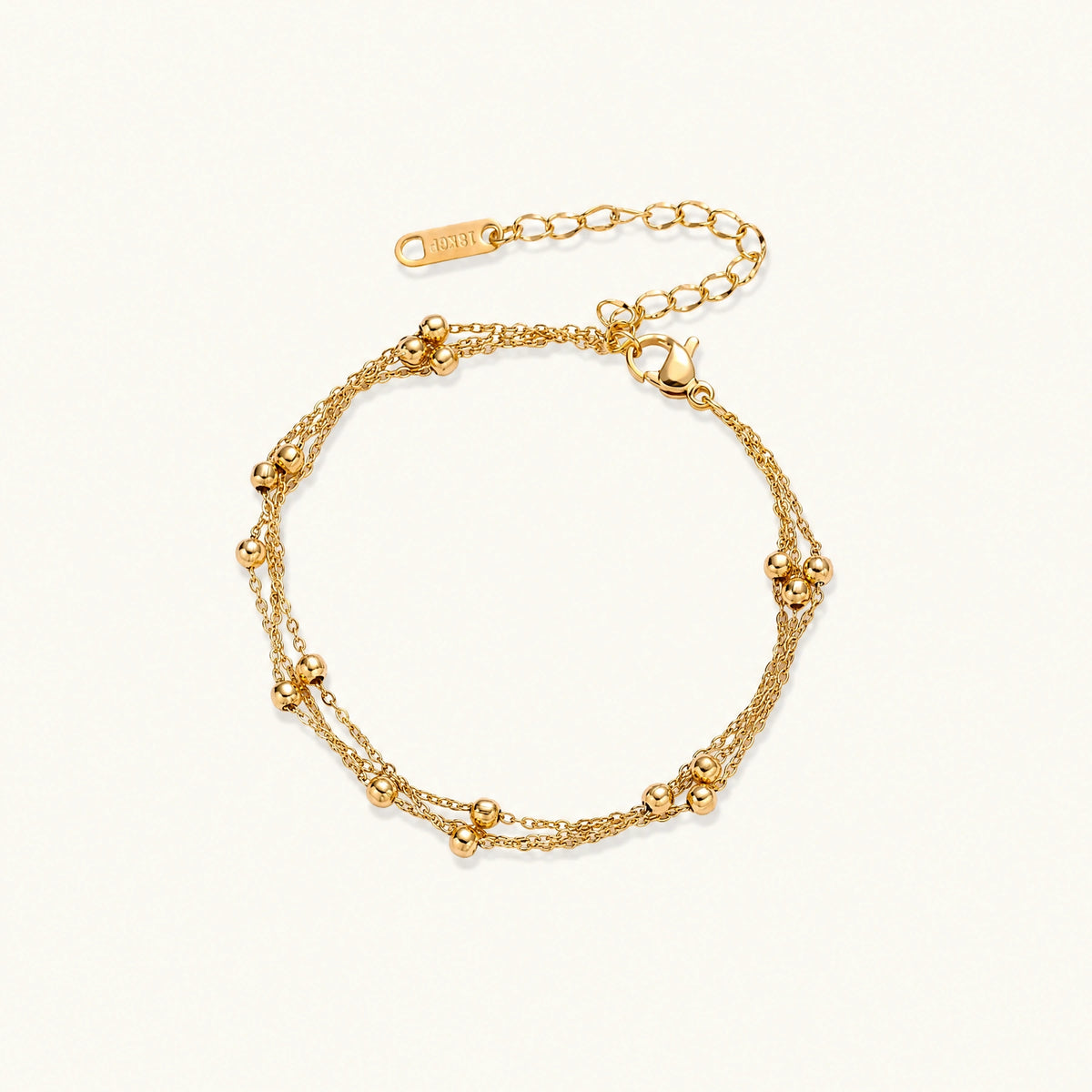 Three-strand gold-plated bracelet with clustered ball beads and adjustable clasp on cream background