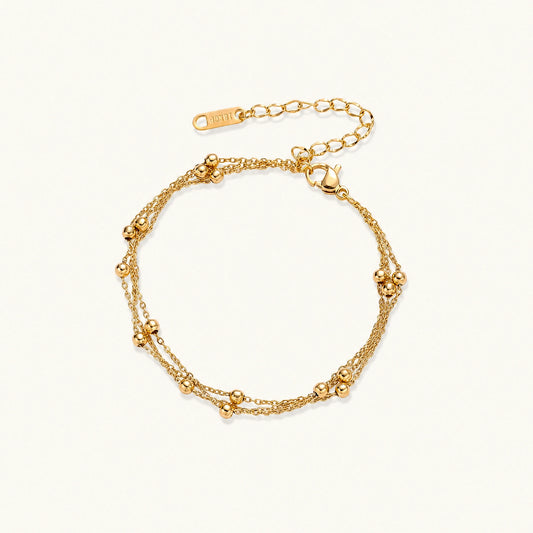 Three-strand gold-plated bracelet with clustered ball beads and adjustable clasp on cream background