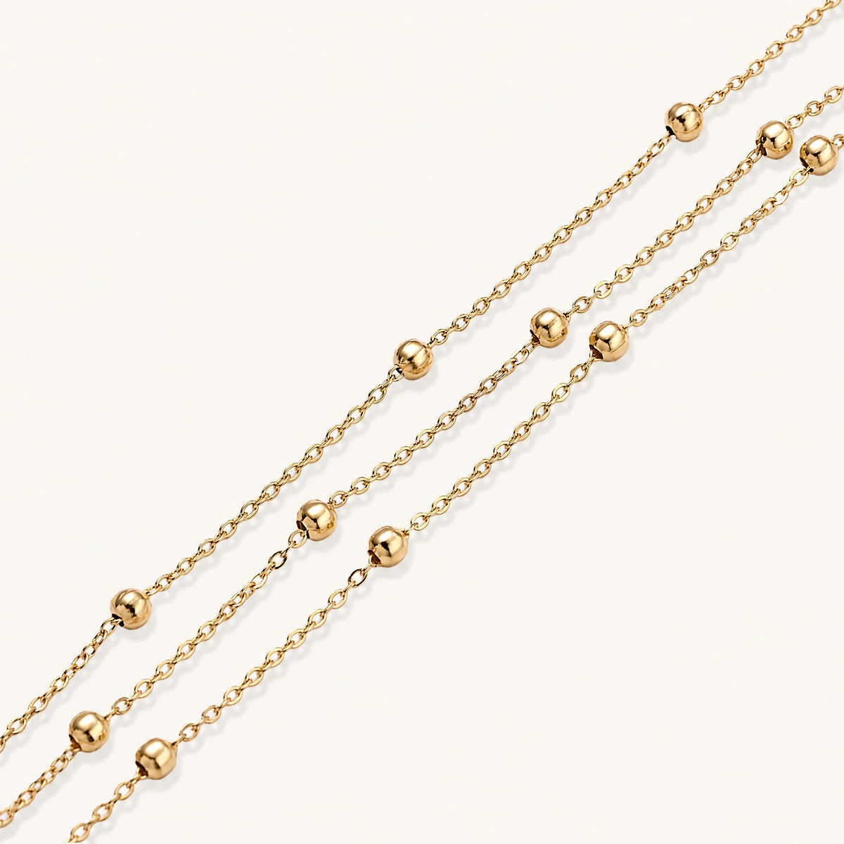 Three-strand gold-plated bracelet with clustered ball beads and adjustable clasp on cream background