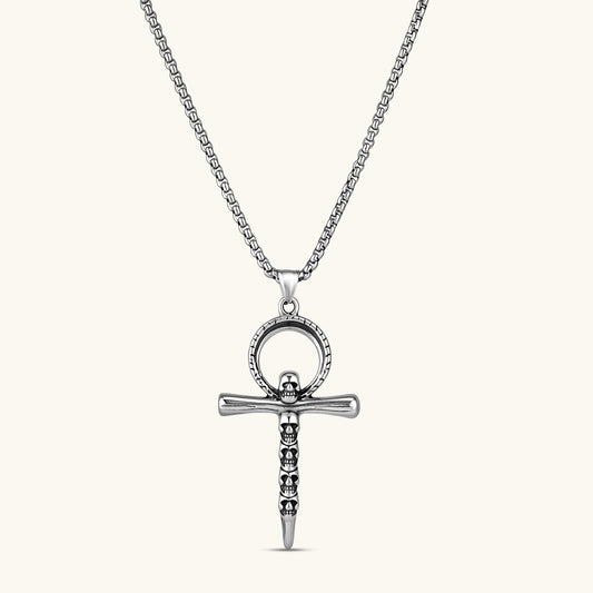 Silver stainless steel ankh pendant with skull motifs on vertical bar and textured ring top, on a box chain necklace.