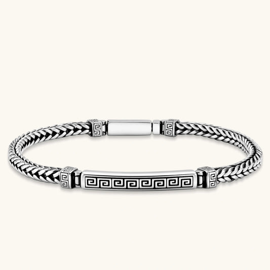 Antique silver plated chain bracelet with a Greek key engraved ID bar and patterned spacer beads on a cream background.
