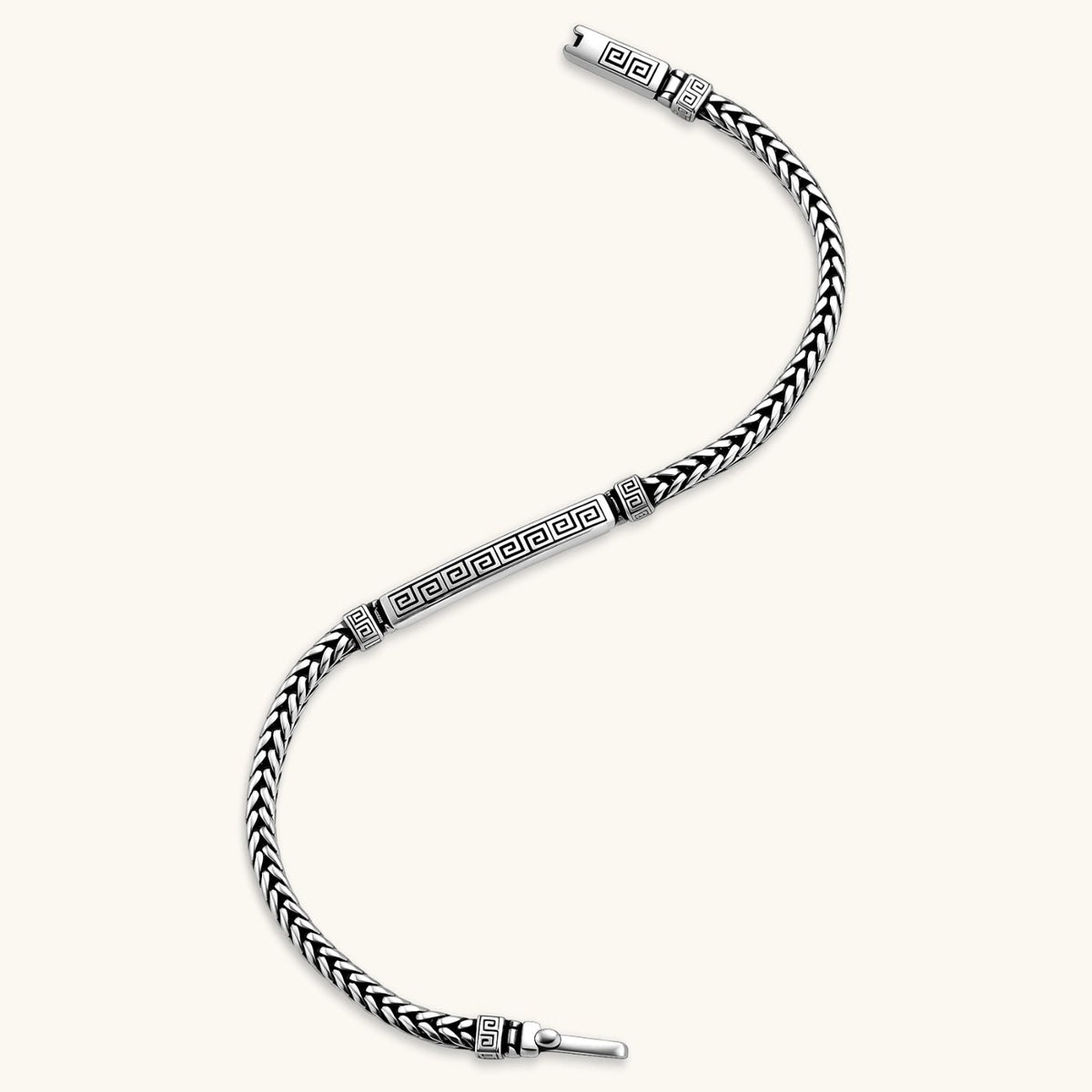 Antique silver plated chain bracelet with a Greek key engraved ID bar and patterned spacer beads on a cream background.